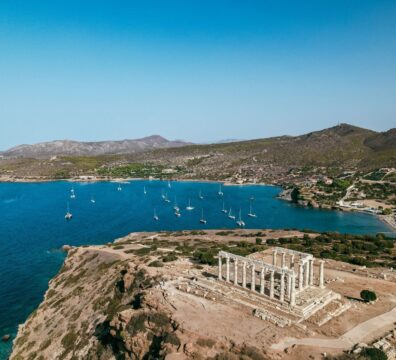 Stunning aerial view of the Temple of Poseidon in Greece with sailboats on the Aegean Sea coastline.