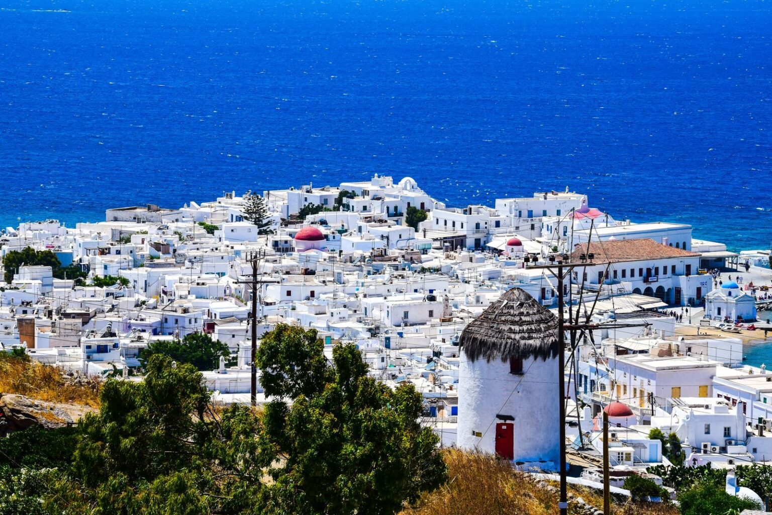 A stunning bird's-eye view of white buildings in Mykonos Town overlooking the blue Aegean Sea.