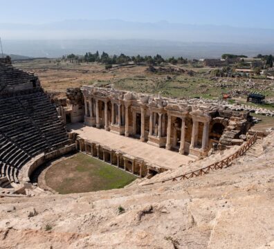 Aerial view of a historic Roman amphitheater in a vast outdoor landscape.