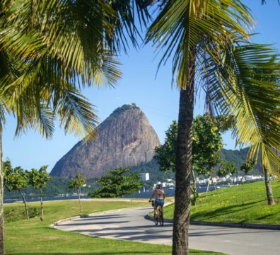 A cyclist rides through a park with a view of the iconic Sugarloaf Mountain in Rio de Janeiro.