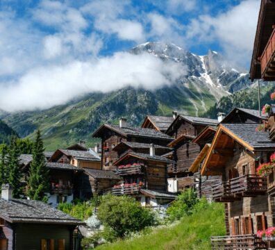 brown wooden houses near green trees and mountain under white clouds during daytime