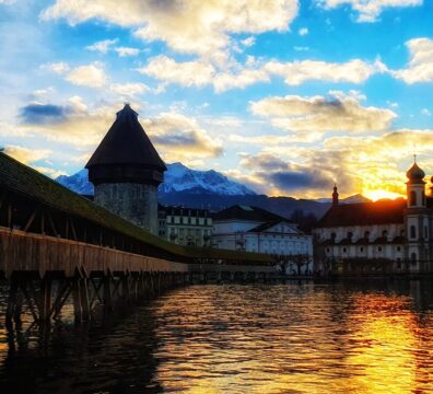 the sun is setting over a lake with a building in the background
