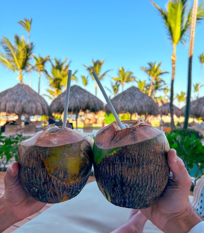 A person holding two coconuts in front of a beach